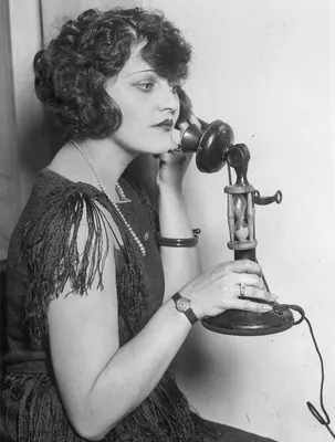 A woman speaking into an early candlestick telephone