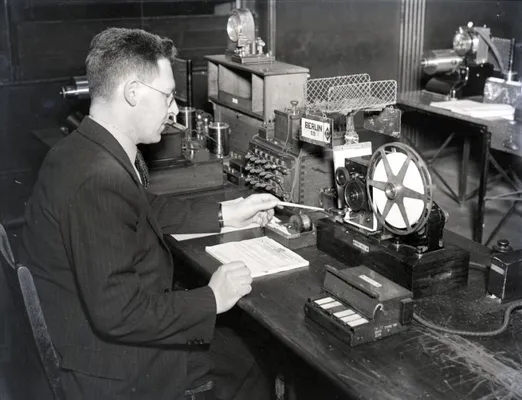 A telegraph operator at a desk, reading paper tape from the machine